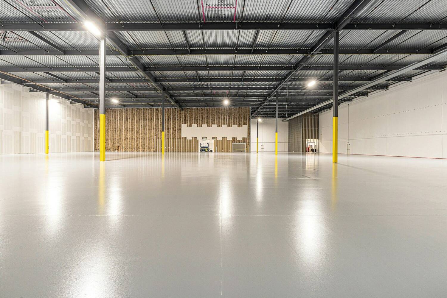 Interior de hală industrială, gol și luminos, cu pardoseală din beton lucios și stâlpi de oțel